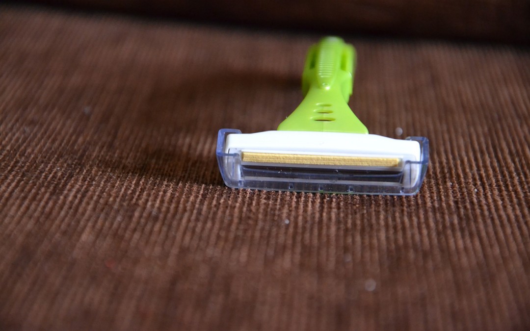 A disposable safety razor with a lime green handle on a brown corduroy surface.
